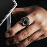 Detailed close-up of a hand wearing an octopus tentacle ring holding playing cards. Dramatic lighting accentuates intricate jewelry design.