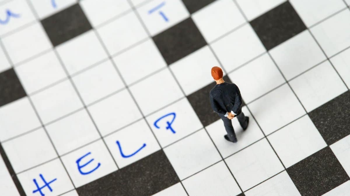 Tiny figurine searching for answers on a crossword puzzle with 'Help' written.