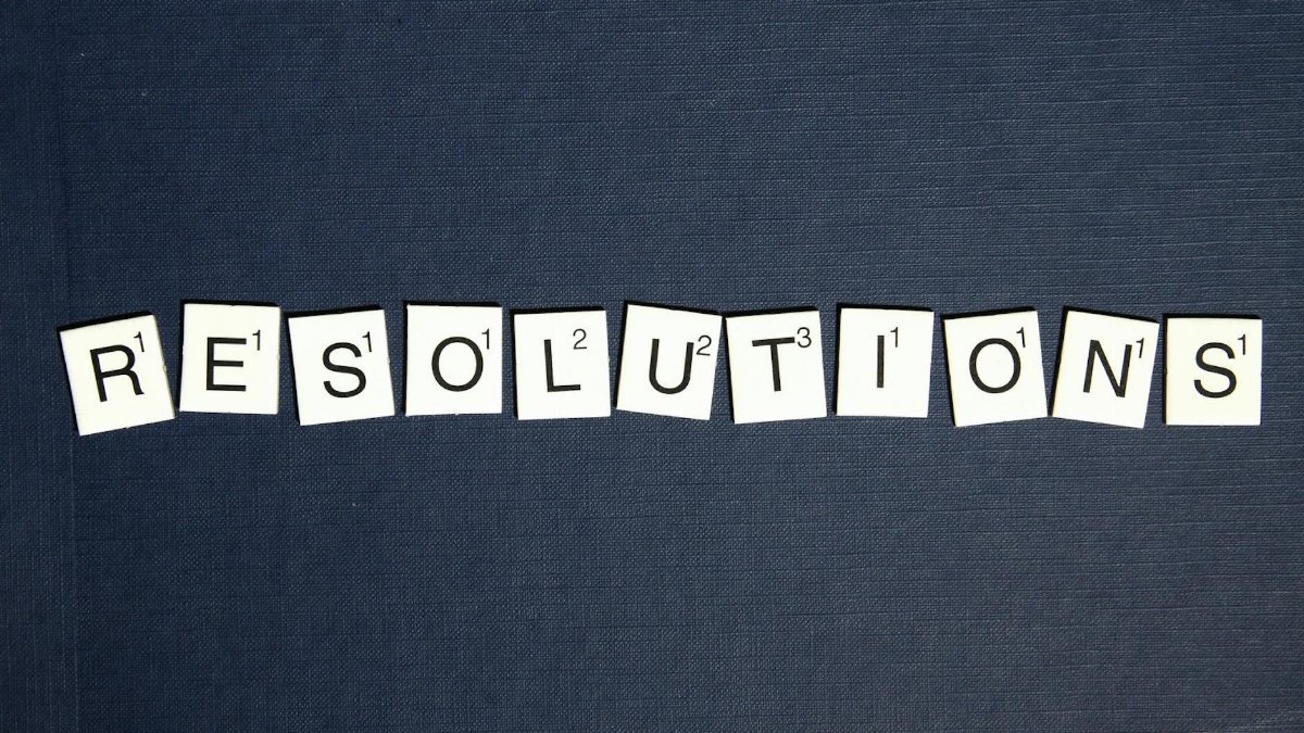 Scrabble tiles spell 'RESOLUTIONS' on a textured dark blue background, capturing a New Year theme.