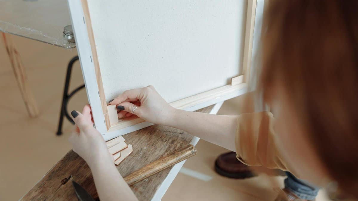 Close-up of hands assembling a canvas frame for a painting project indoors.