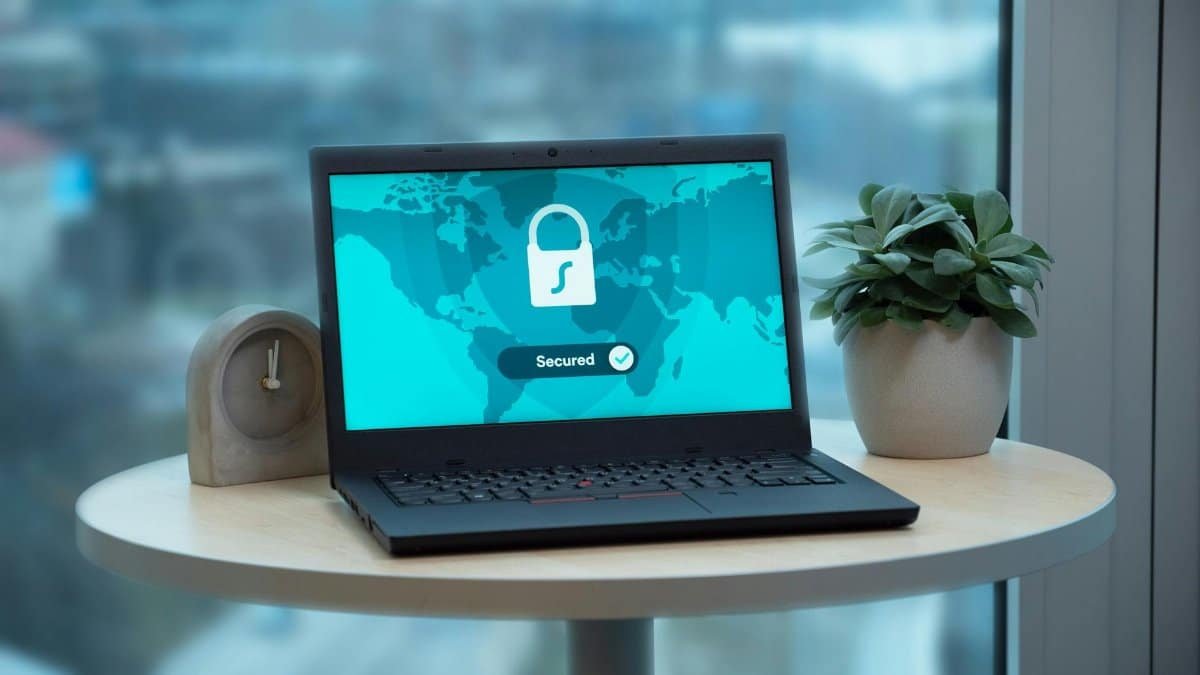 Laptop displaying a security lock icon on a table with a potted plant and clock.