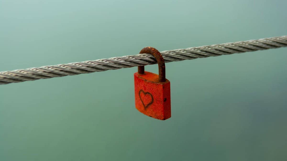 A rusty padlock with a heart hanging on a wire, symbolizing love or security.