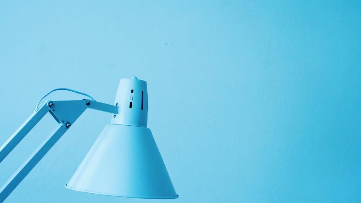 Close-up of a minimalist desk lamp against a light blue background with ample copy space.