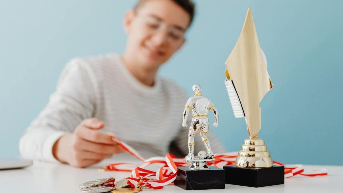 Teenage boy sitting with soccer trophy, medals, and award cup, smiling.