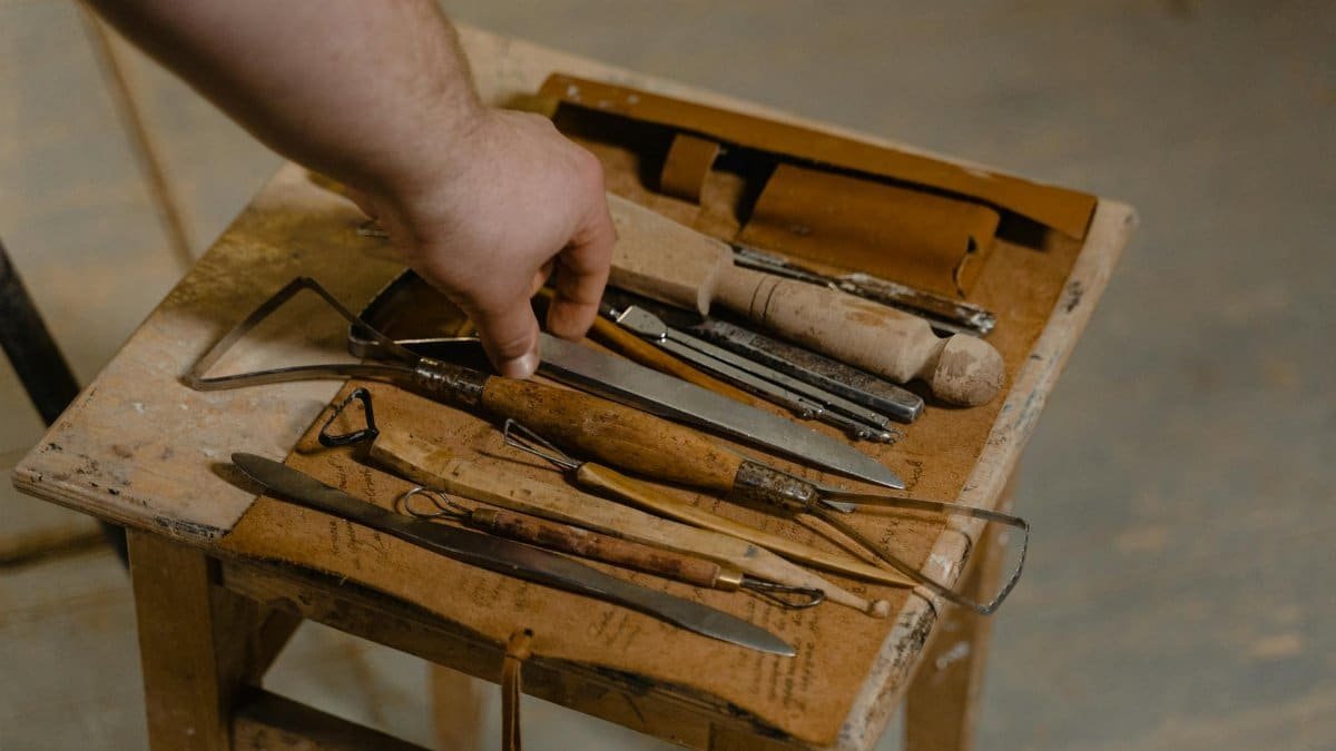A close-up of artisan hand selecting tools on a wooden stool for woodwork.