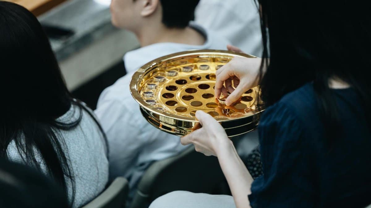 A golden communion plate is passed during a church service, reflecting the act of worship.
