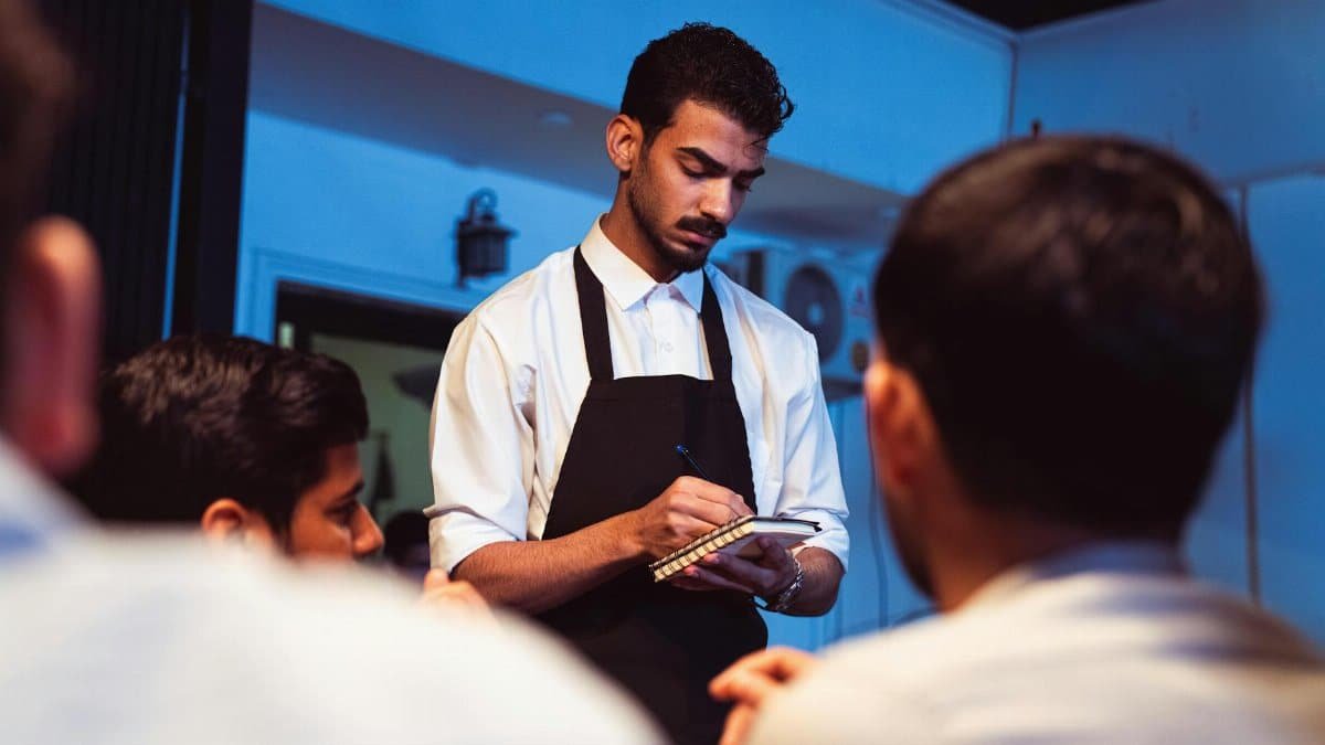 Attentive waiter writing down a customer's order in a cozy indoor restaurant.