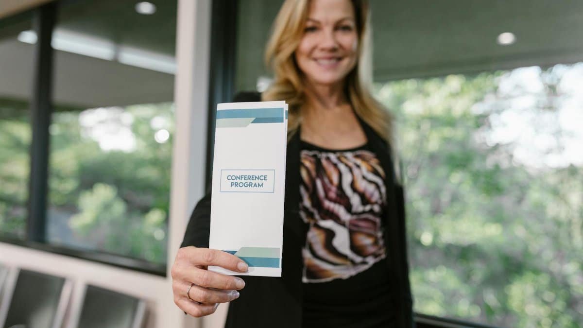 Woman holding a conference program flyer indoors with a blurred background.