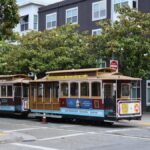 Classic San Francisco cable car on Powell and Mason, city streets, greenery, and iconic signs.
