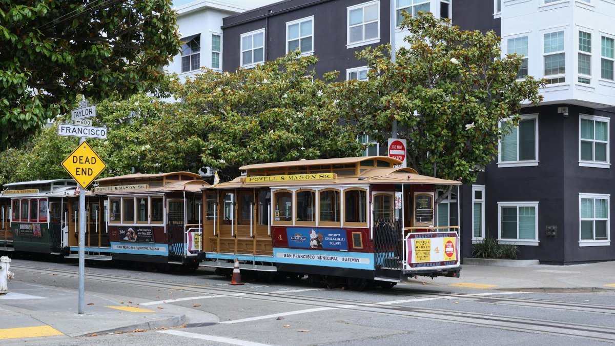 Classic San Francisco cable car on Powell and Mason, city streets, greenery, and iconic signs.