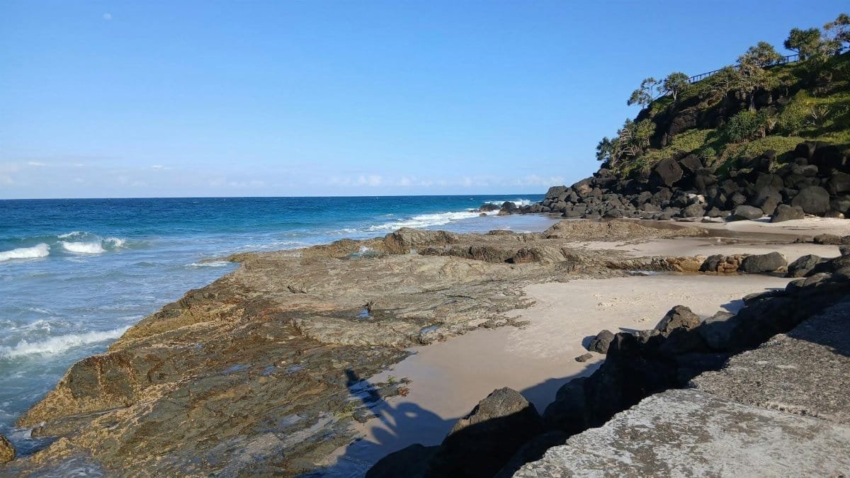 A tranquil beach scene with rocky shoreline and ocean waves under a clear blue sky.