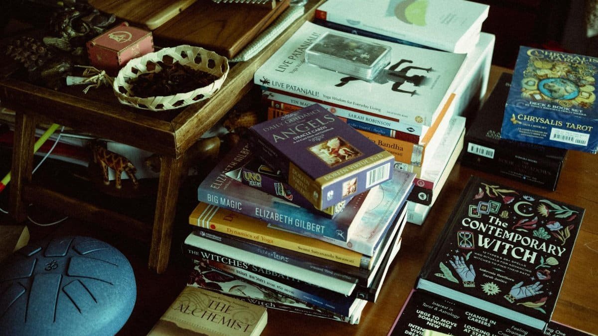 A diverse assortment of books, tarot cards, and spiritual items arranged on a cluttered table.