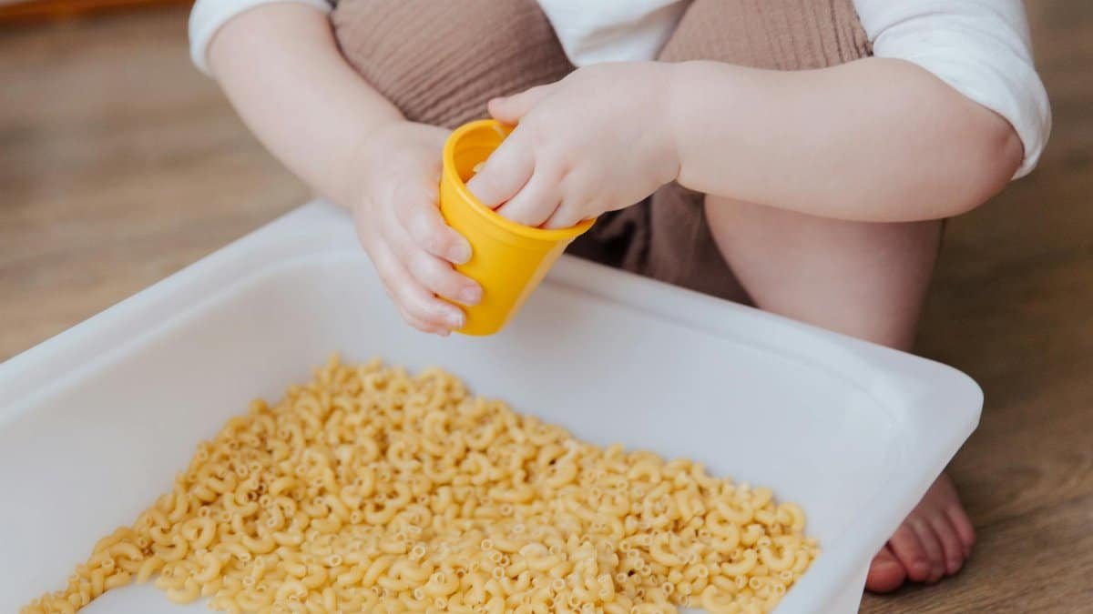 A young child plays with dry macaroni in a sensory activity, enhancing creativity and learning.