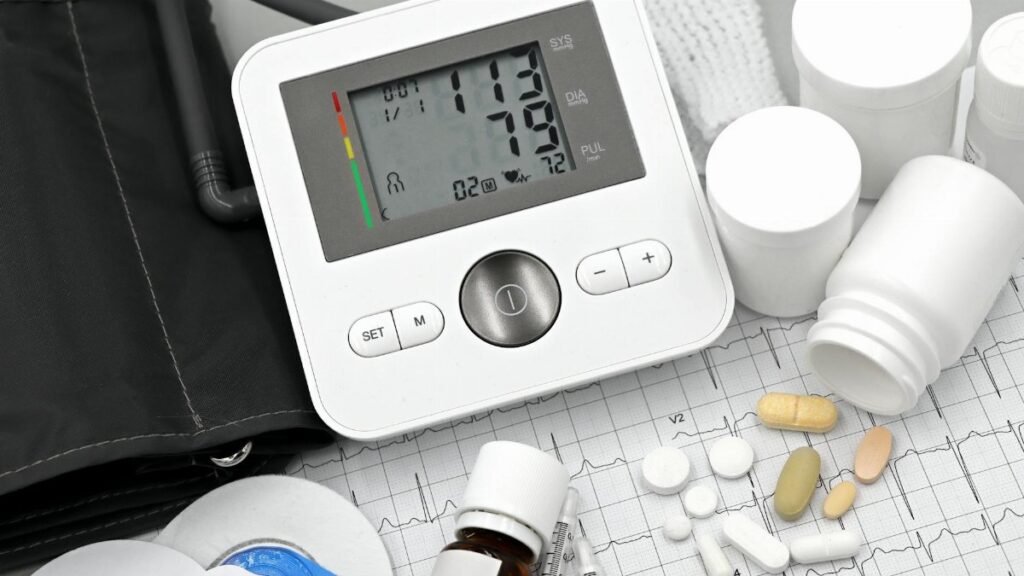 Digital blood pressure monitor on ECG paper with pills and medical supplies, ideal for healthcare topics.