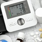 Digital blood pressure monitor on ECG paper with pills and medical supplies, ideal for healthcare topics.