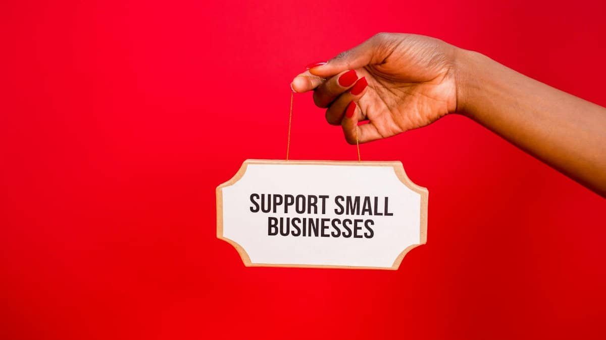 A hand holds a sign that reads 'Support Small Businesses' against a vibrant red background.