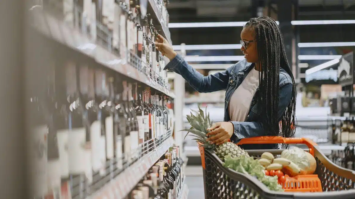 A woman shopping for wine and groceries, filling her cart with fresh produce.