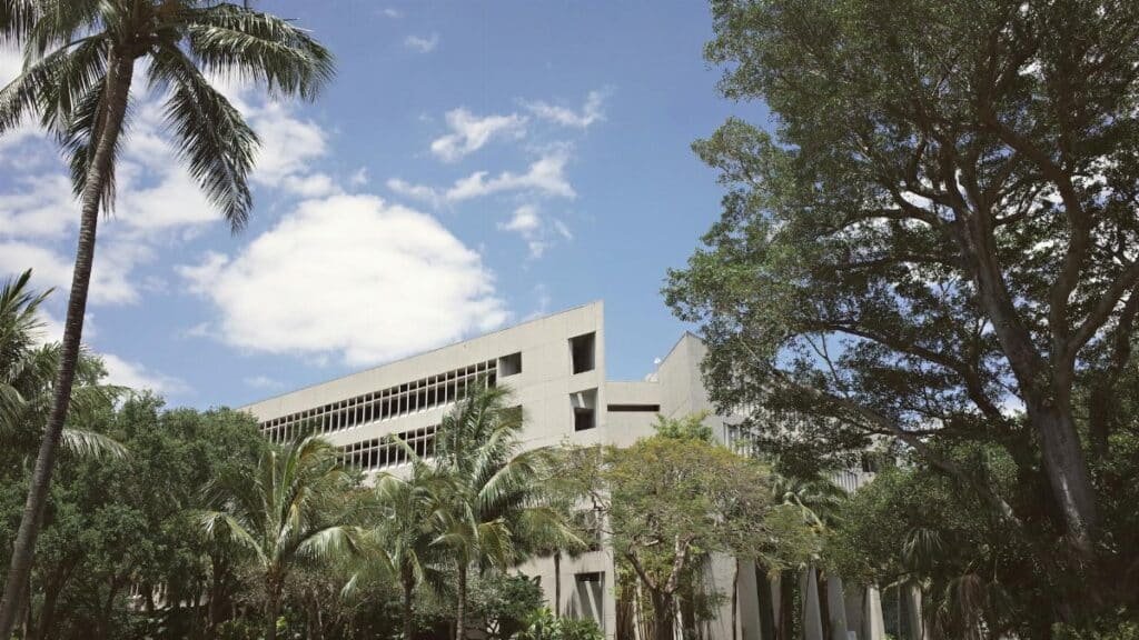 A sunny view of a modern university campus in Coral Gables, Florida, surrounded by palm trees and greenery.