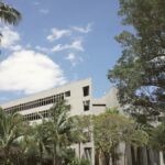 A sunny view of a modern university campus in Coral Gables, Florida, surrounded by palm trees and greenery.