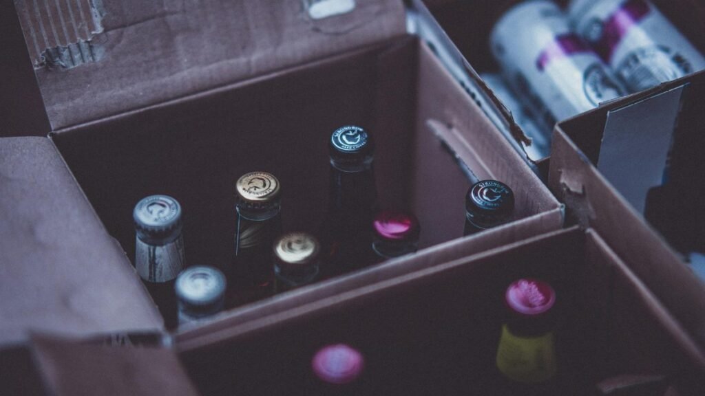 Close-up of various alcohol bottles and cans in cardboard boxes indoors.