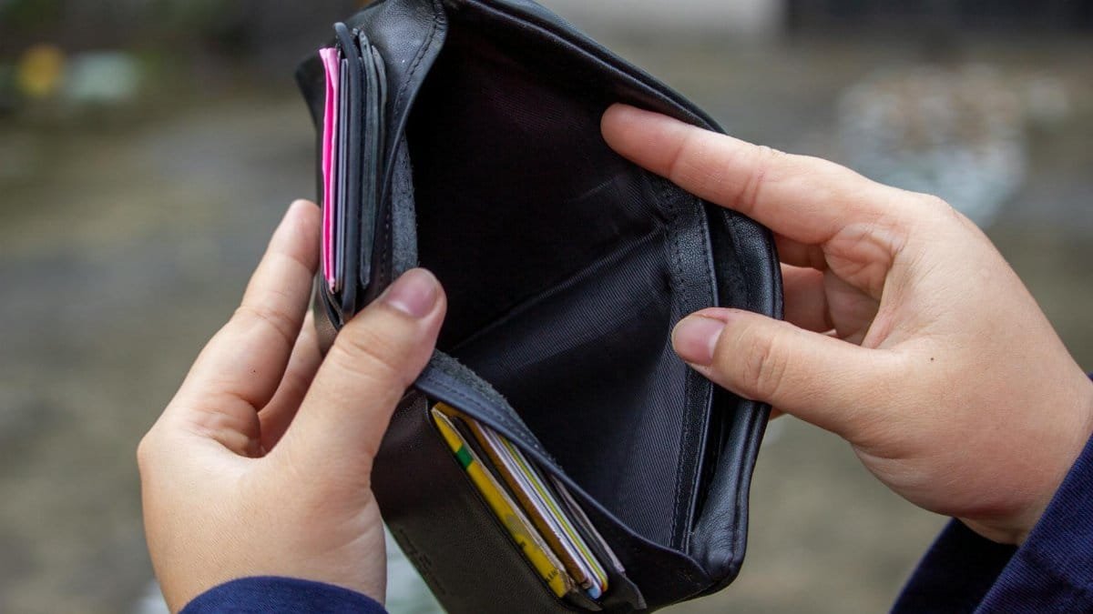 An outdoor image of hands holding an empty black wallet, suggesting financial scarcity.