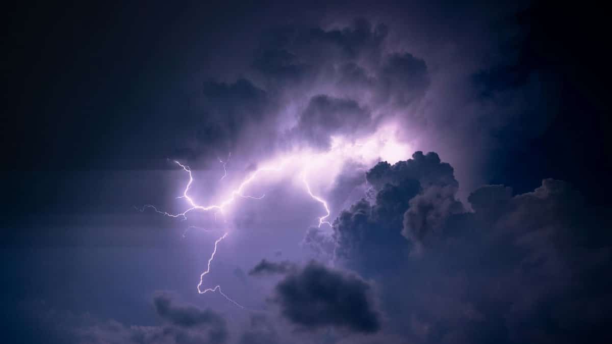 A powerful lightning bolt illuminates dark storm clouds, creating a dramatic and moody sky scene.