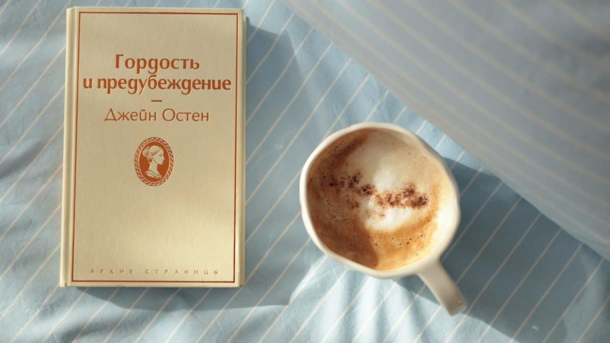 A calm morning scene with a cup of coffee and a book on a striped bedsheet.