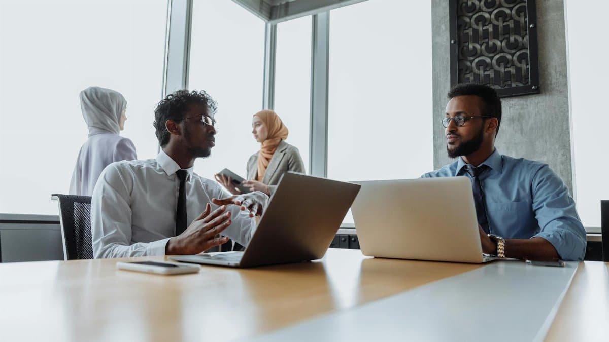 A diverse team of professionals engaged in a business meeting in a modern office environment with laptops and devices.