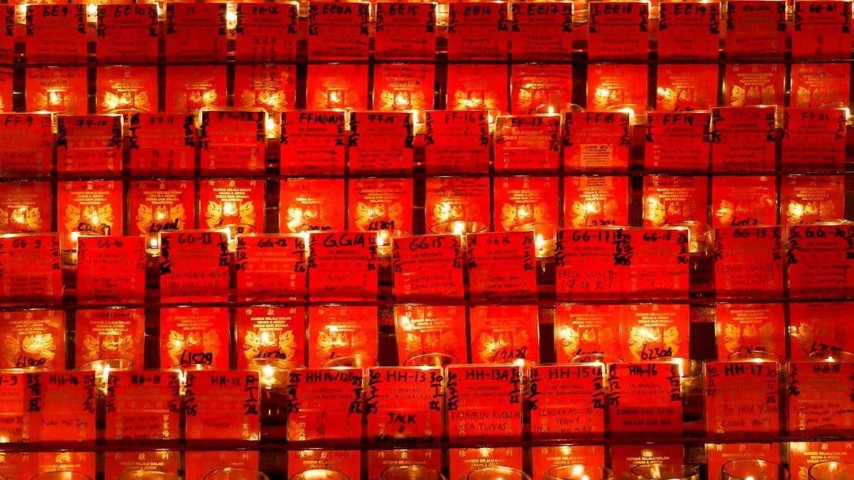A collection of votive candles set against a wall of red cards, creating a warm and spiritual ambiance.