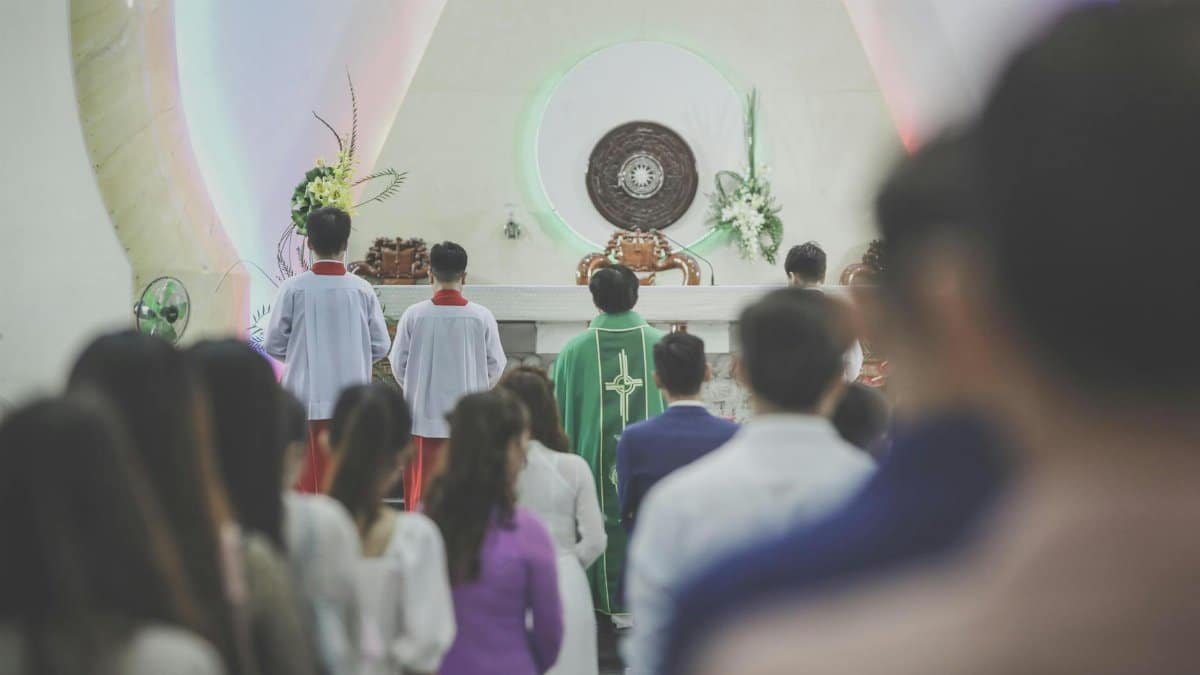 A group of people participating in a Catholic mass ceremony in a church, led by a priest in green vestments.