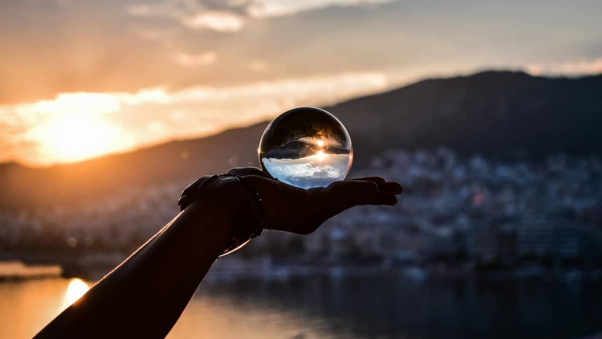 Hand holding a crystal ball capturing a stunning sunset over a cityscape, creating a magical reflection.
