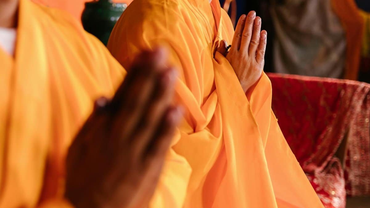 Monks in traditional orange robes meditating with prayer hands.