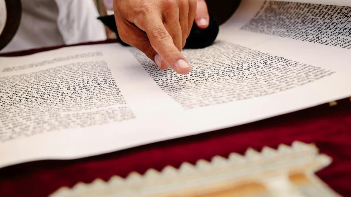 A close-up view of a hand pointing to text on an ancient religious scroll, indicating reading and study.