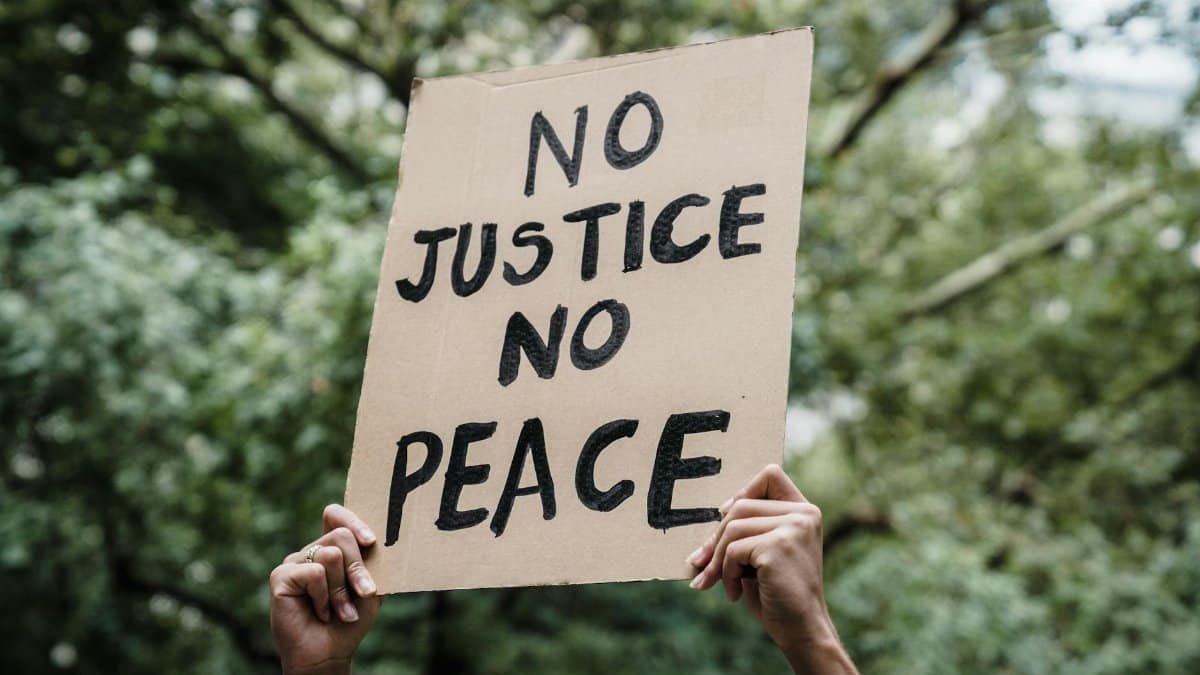 Close-up of a protest sign reading 'No Justice No Peace' held up outdoors. Focus on activism.