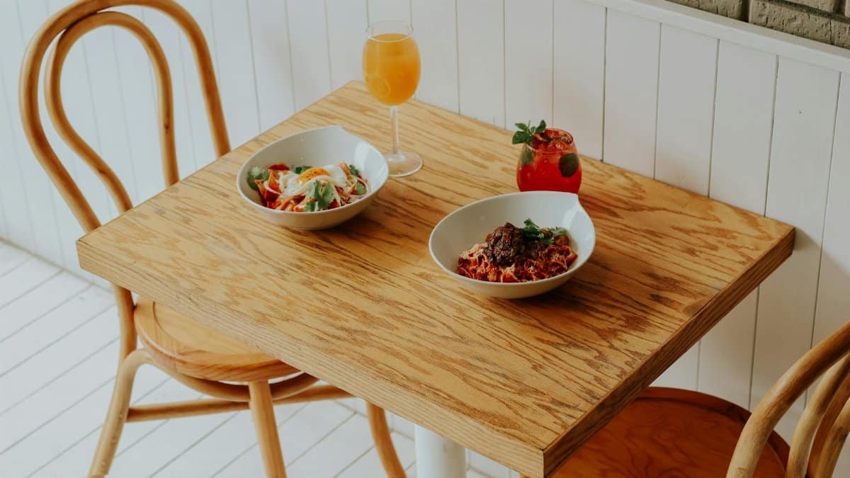 Two bowls of fresh dishes with drinks on a rustic wooden table in a cozy bistro setting.