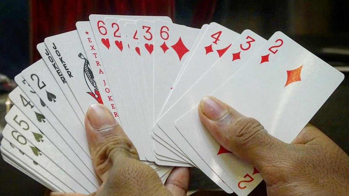 Focused view of hands holding playing cards, emphasizing a mix of clubs, hearts, and jokers.