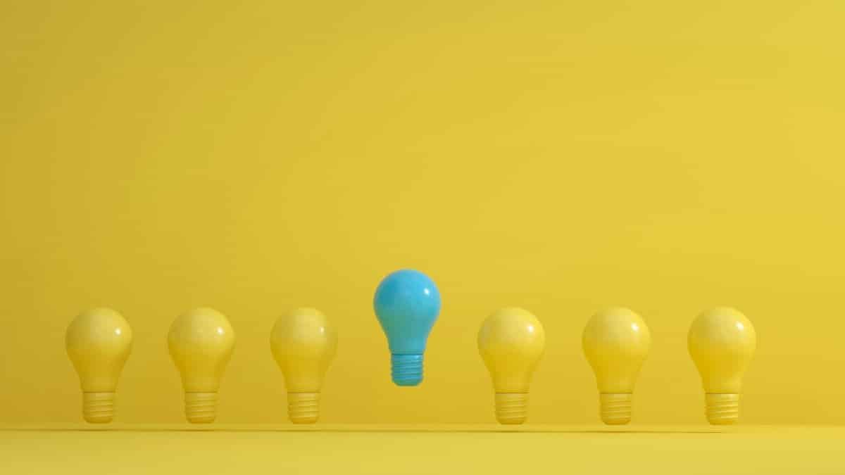 A standout blue light bulb among several yellow bulbs on a yellow background, symbolizing innovation.