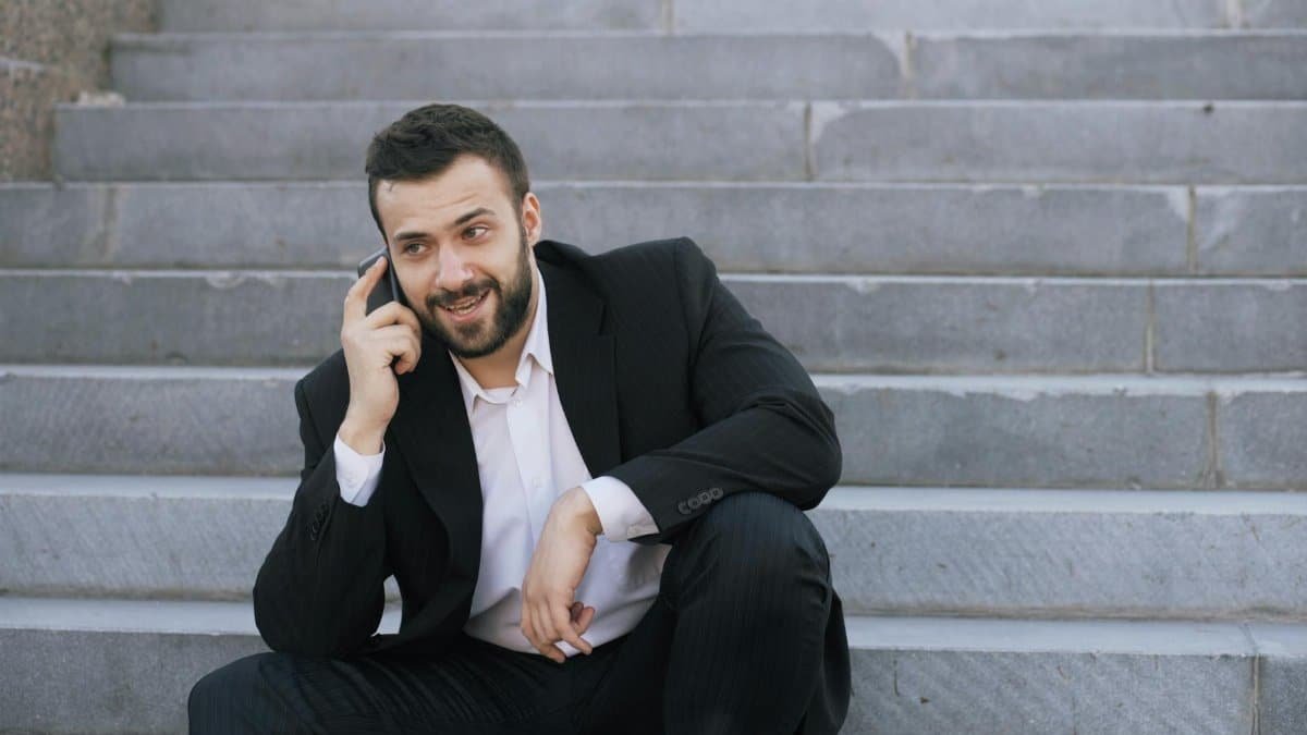 A cheerful businessman in a suit sitting on steps, talking on a mobile phone outdoors.
