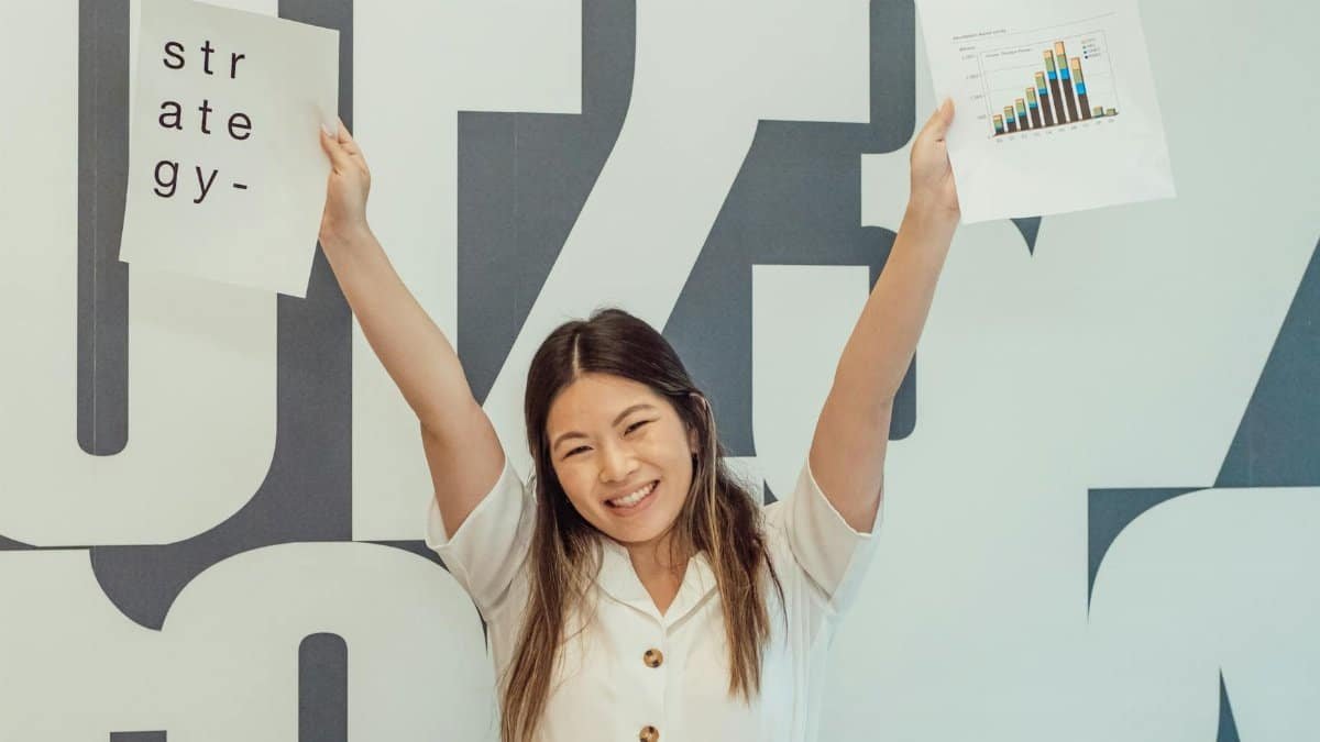 Smiling woman raises hands with strategy and graph papers, celebrating business success.