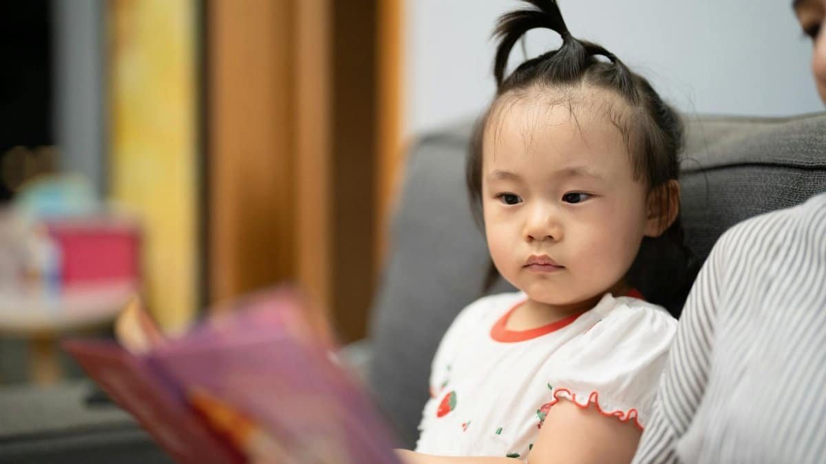 A young child on a sofa attentively listening during a reading session indoors.