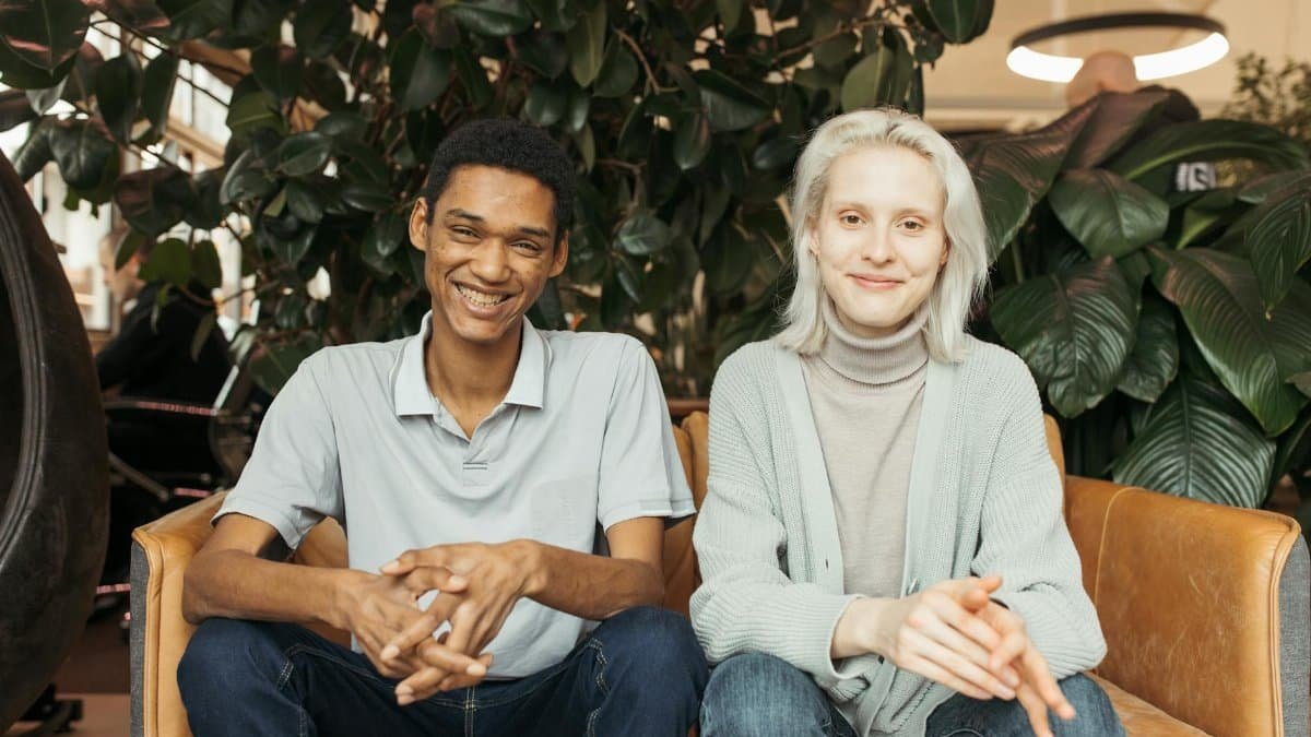 Two young adults smiling and sitting comfortably on a modern couch indoors.