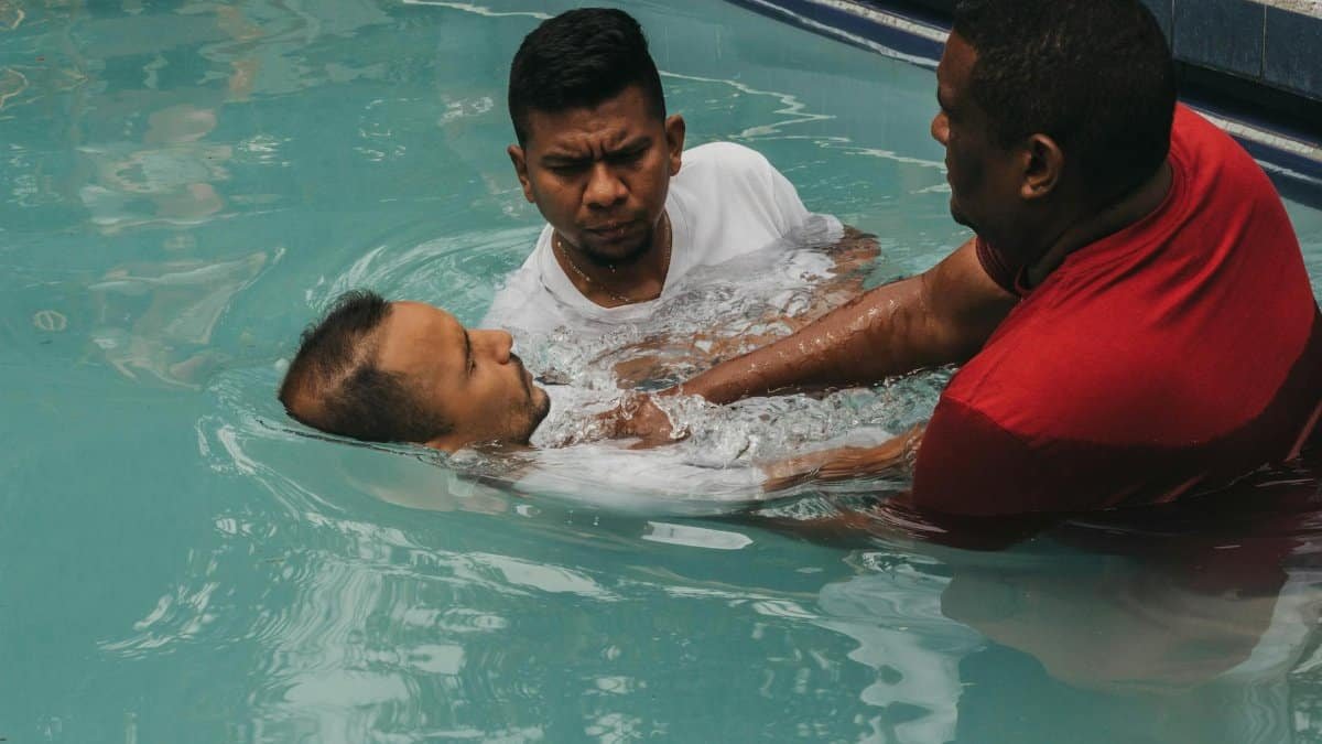 Three men performing a baptism in a swimming pool, symbolizing faith and tradition.