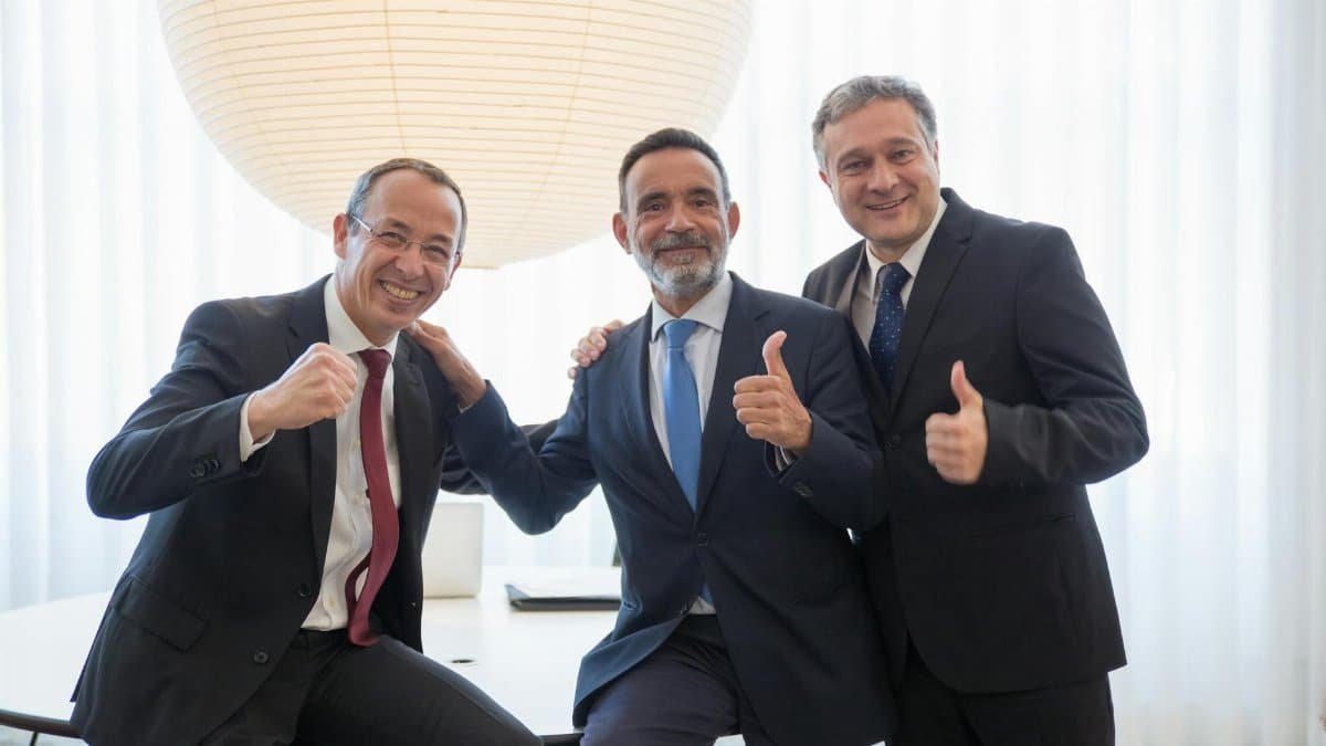 Three businessmen in suits smiling and giving thumbs up, symbolizing team success and positivity.