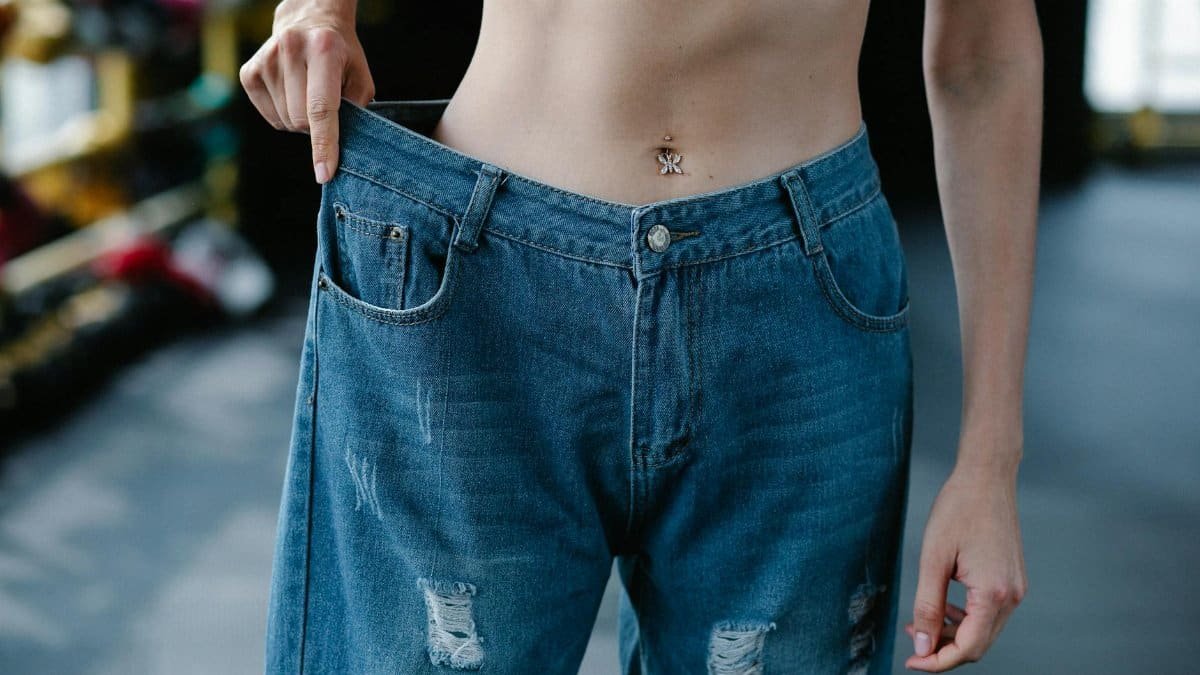 A woman showcases significant weight loss results confidently wearing loose jeans.