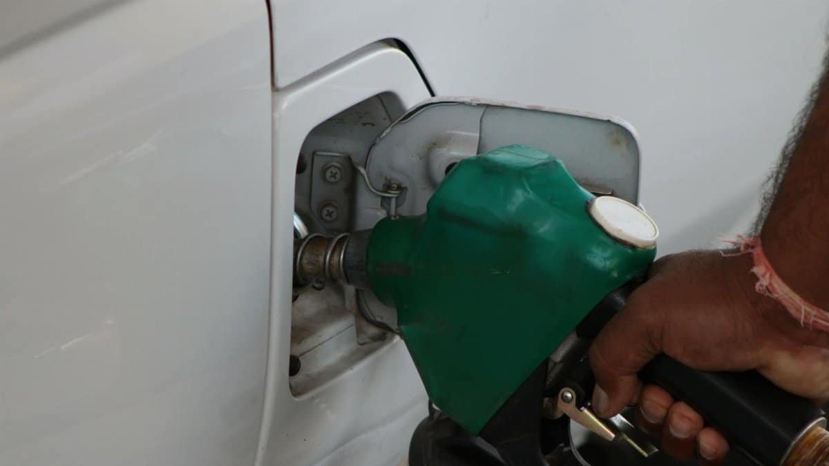 Close-up of a hand refilling a car's gas tank at a station with a green fuel nozzle.