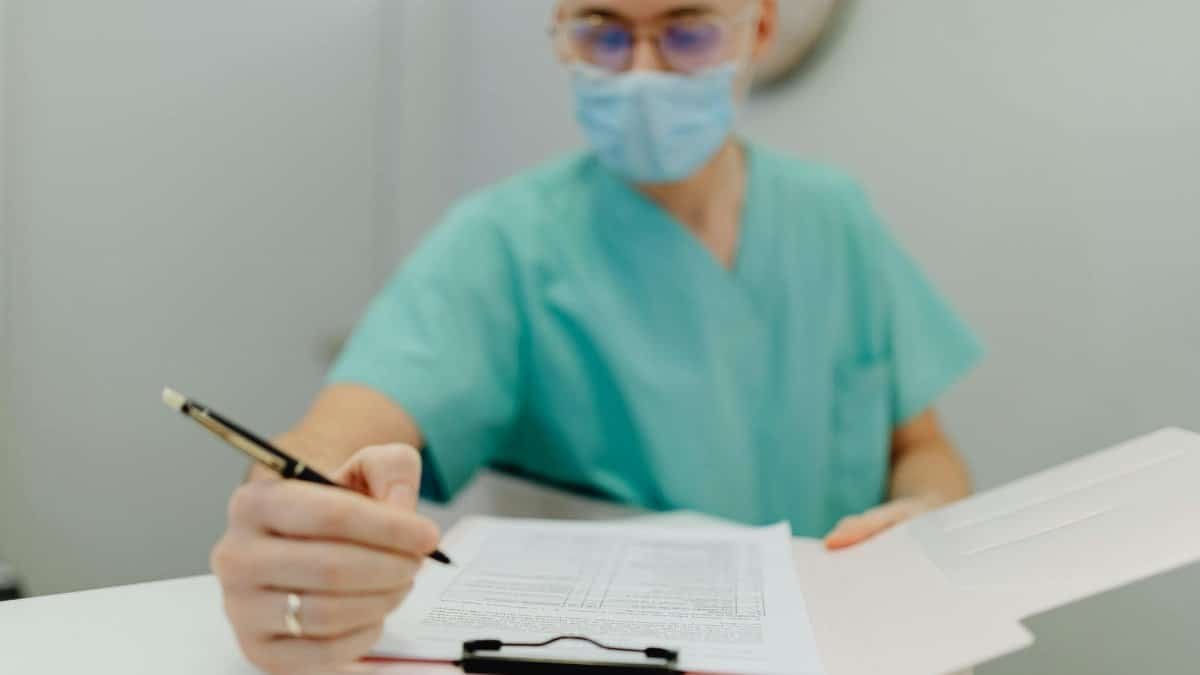 Medical practitioner wearing mask writes notes on clipboard, emphasizing patient care and safety.