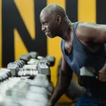 Strong senior man focusing on strength training with dumbbells in a vibrant gym.