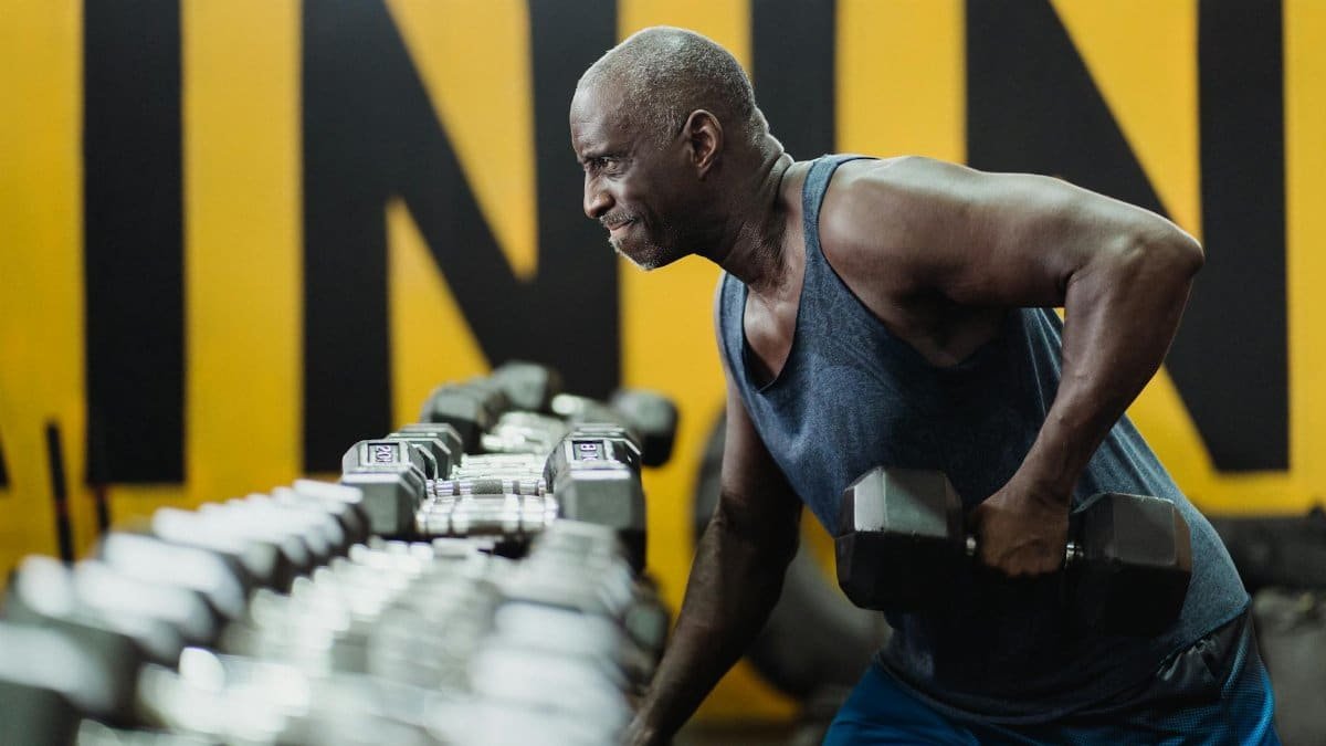 Strong senior man focusing on strength training with dumbbells in a vibrant gym.