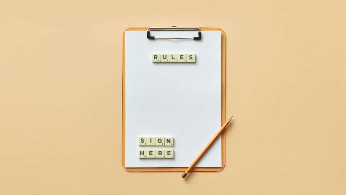 Flat lay of clipboard with letter tiles spelling 'rules' and 'sign here', accompanied by pencil on beige background.