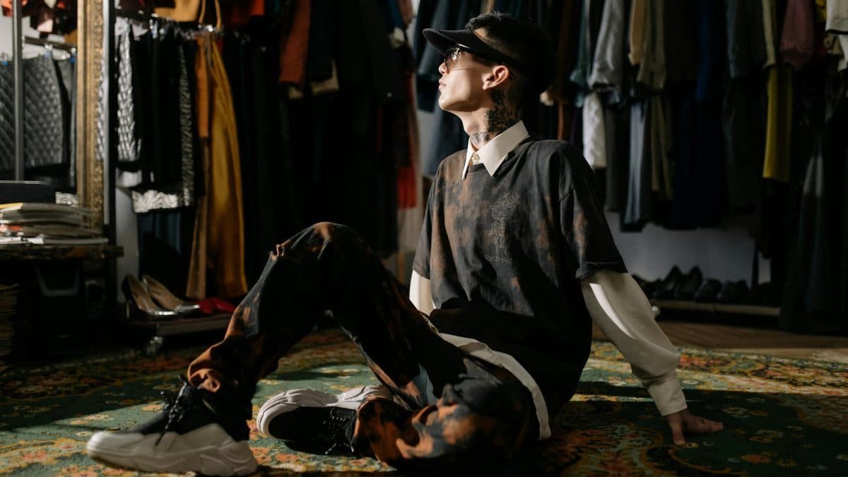 Young man in a vintage clothing showroom, seated on a patterned carpet, looking stylish and modern.